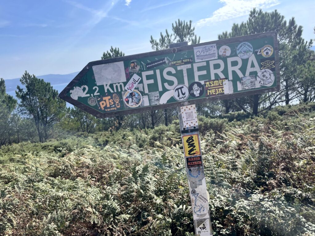 Signpost back to Finisterre centre of town from the lighthouse and whose sticker coverage gives a flavour of the alternative vibe at the place. 